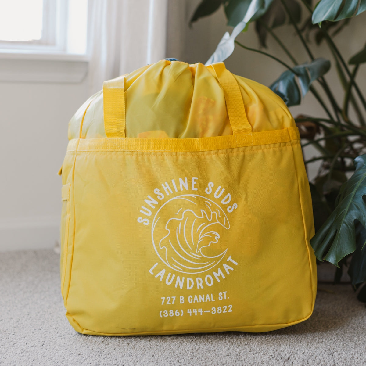 A yellow laundry bag with the logo and contact information for Sunshine Suds Laundry.