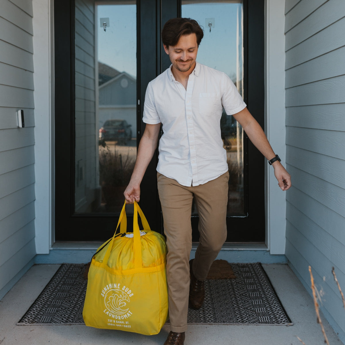 A man carrying a yellow laundry bag out his door